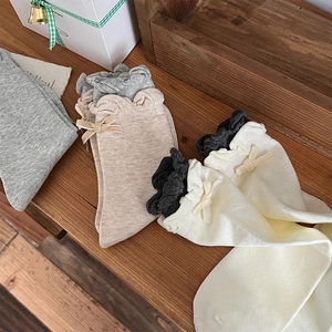 Detailed view of color-block knit socks with ruffle edges and velvet bows on wood
