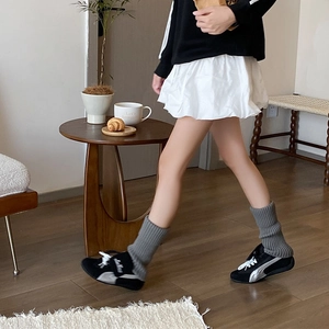 Detail of grey knitted leg warmers styled with black sneakers and a white pleated skirt