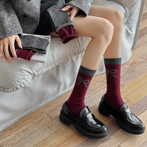 Detail view of burgundy knitted socks with gray bow patterns and ribbed cuffs worn by a model
