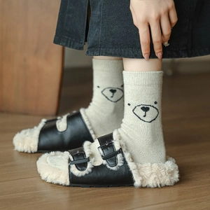 Pantoufles en cuir noir avec doublure polaire et chaussettes ours sur parquet