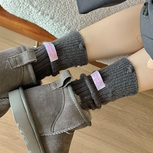 Close-up of dark grey ribbed socks with pink 'Handmade' tag paired with grey suede boots