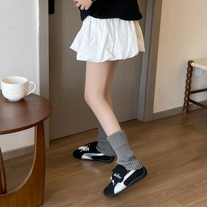 Detail of black suede sneakers with silver stripes paired with gray knitted leg warmers