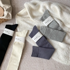 Chaussettes montantes en coton peigné aux tons neutres disposées sur un tapis en fourrure