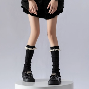 Détail de jambières noires en tricot avec bordure en dentelle blanche et nœuds en soie