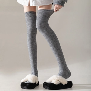 Détail de chaussettes hautes grises à côtes portées avec des pantoufles en peluche