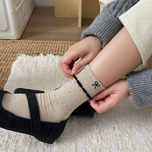 Close-up of beige knit socks featuring black wave trim and bow embroidery details