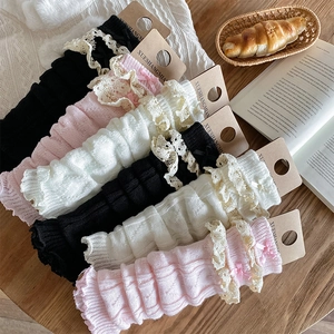 Trois paires de jambières avec dentelle et nœuds en noir, blanc et rose sur un bureau en bois