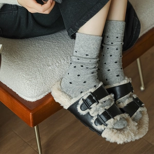 Close-up of black double-buckle plush slippers paired with grey polka dot wool socks