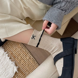 Detail of ruffled lace trim and black bow embroidery on beige ribbed cotton socks