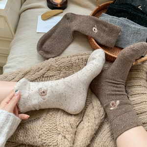 Detail of speckled wool socks featuring cute bear embroidery and cozy knitted texture
