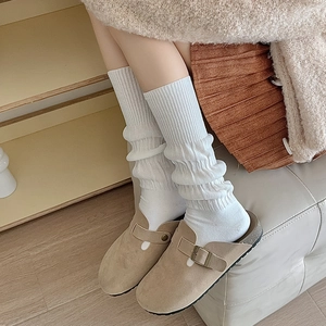 Detail of beige suede mule shoe with bronze buckle and white ribbed knitted socks