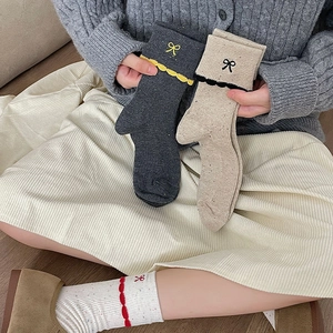 Close-up of lace cuffs on ribbed crew socks featuring delicate bow embroidery detail
