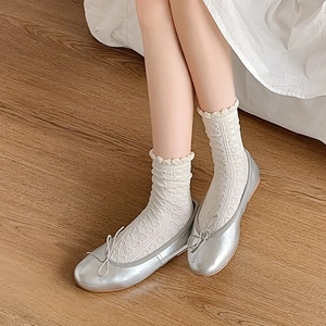 Nahaufnahme silberner Ballerinas mit Schleife und weißen Spitzensocken mit Schmetterlingsmuster