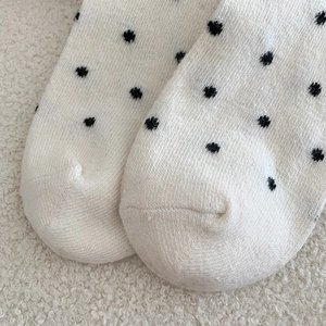 Close-up of cream knit wool socks with black polka dots on a soft cozy background