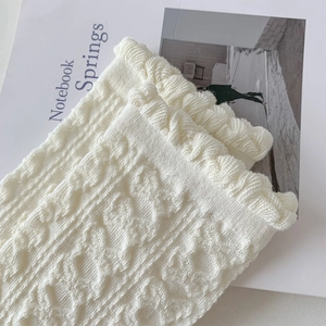 Nahaufnahme cremeweißer Stricksocken mit Reliefmuster und gerüschten Spitzenkanten