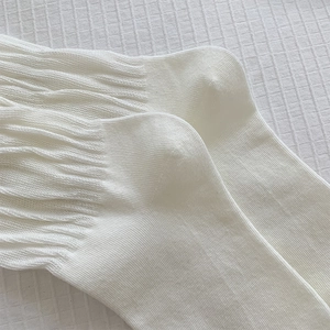 Detail of white slouch socks with ribbed knit texture on a soft quilted fabric background
