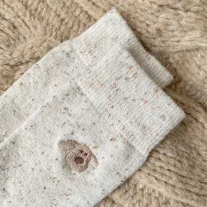 Detail of oatmeal wool socks with colorful flecks and a cute brown dog embroidery