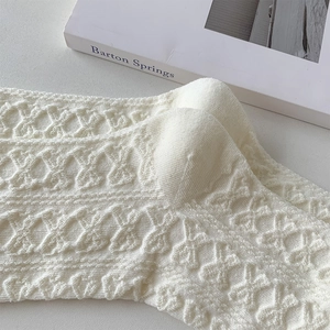 Nahaufnahme cremeweißer Stricksocken mit feiner Lochspitze und zartem Rautenmuster-Design