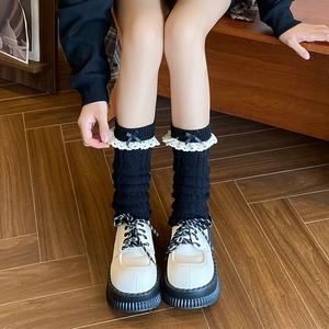 Détail de jambières en tricot noir avec bordure en dentelle blanche et nœud satin