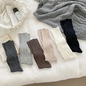 Detailed knit texture of six neutral color slouch socks arranged on a white bed