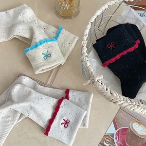 Detail of knit socks featuring colorful flecked yarn, wavy scalloped edges, and bow embroidery