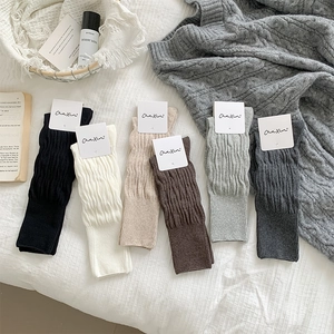 Detail of twisted knit leg warmers in various colors with Chaxin branding on bed