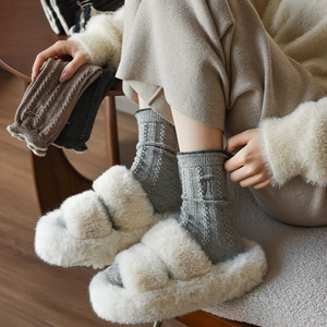 Détail de chaussettes en laine avec broderie nœud et maille torsadée grise avec pantoufles