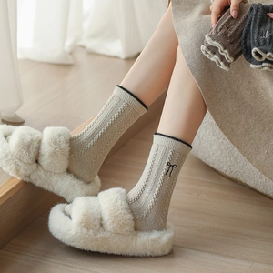 Détail de chaussettes en laine à torsades beiges avec broderie de nœud noir raffiné