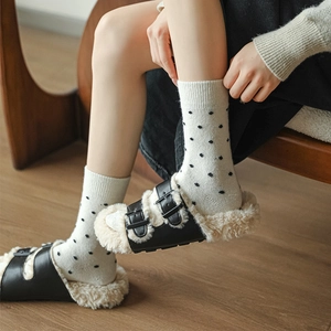 Detail of warm black leather buckle clogs with white faux shearling lining and polka dot socks