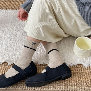 Detail of beige knit mid-calf socks with black bow embroidery and wavy lace trim