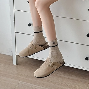 Detail of beige bow socks with black lace trim paired with suede clogs and metal buckle