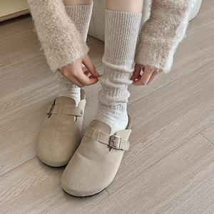 Close-up of stylish beige suede clogs with metallic buckles and vertical ribbed knit socks