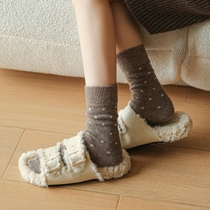 Detail of wool socks with white polka dots worn with cream faux fur slides on wood floor