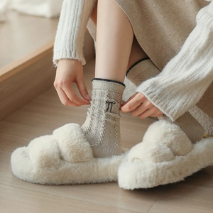 Détail de chaussettes en laine avec broderie nœud et pantoufles en peluche dans un intérieur