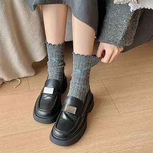 Detail of grey wool socks with blue bow embroidery and ruffle edge styled with black loafers