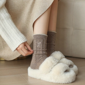 Détail de chaussettes en laine marron avec broderie nœud blanc et maille torsadée