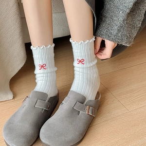 Detail of white wool socks with red bow embroidery and suede clog slippers