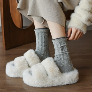 Sandales d'hiver en fausse fourrure crème et chaussettes en maille grise sur bois