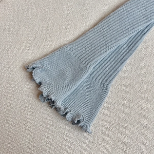 Détail de jambières en tricot bleu clair avec bords ondulés et texture côtelée