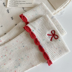 Detailed view of white knitted socks with colorful flecks, red bow embroidery and ruffle trim