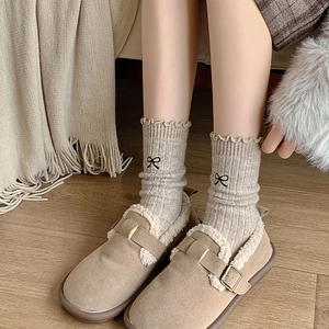 Detailed view of beige wool socks with bow embroidery and ruffled cuffs worn with warm shoes