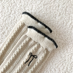 Détail de chaussettes en laine beige avec broderie nœud noir et texture torsadée