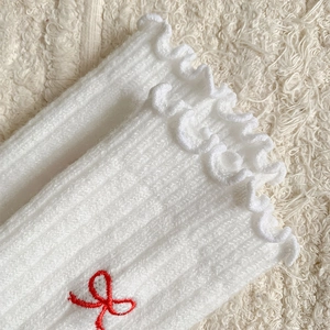 Close-up of white ribbed wool socks featuring ruffled edges and red bow embroidery