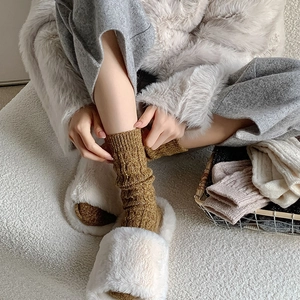 Detail shot of caramel cable knit wool socks paired with plush slippers in warm home setting