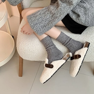 Detail of cream faux fur mules with brown leather buckle and cork sole on grey socks
