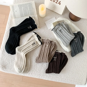 Détail de chaussettes en laine avec broderie nœud et bords à volants tons neutres