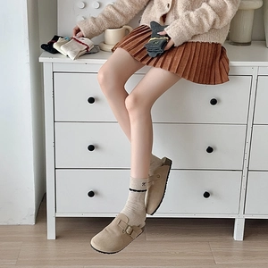 Close-up of ballet style bow embroidery on knit socks paired with suede clogs