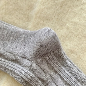 Macro view of light grey wool socks featuring thick cable knit texture and reinforced heel