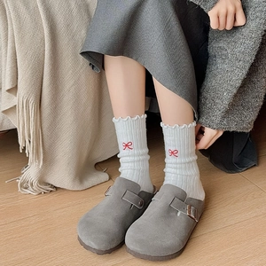 Detailed view of white ruffle socks with red bow embroidery and grey suede clogs
