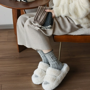 Détail de chaussettes en laine brodées et de pantoufles en peluche sur un sol en bois
